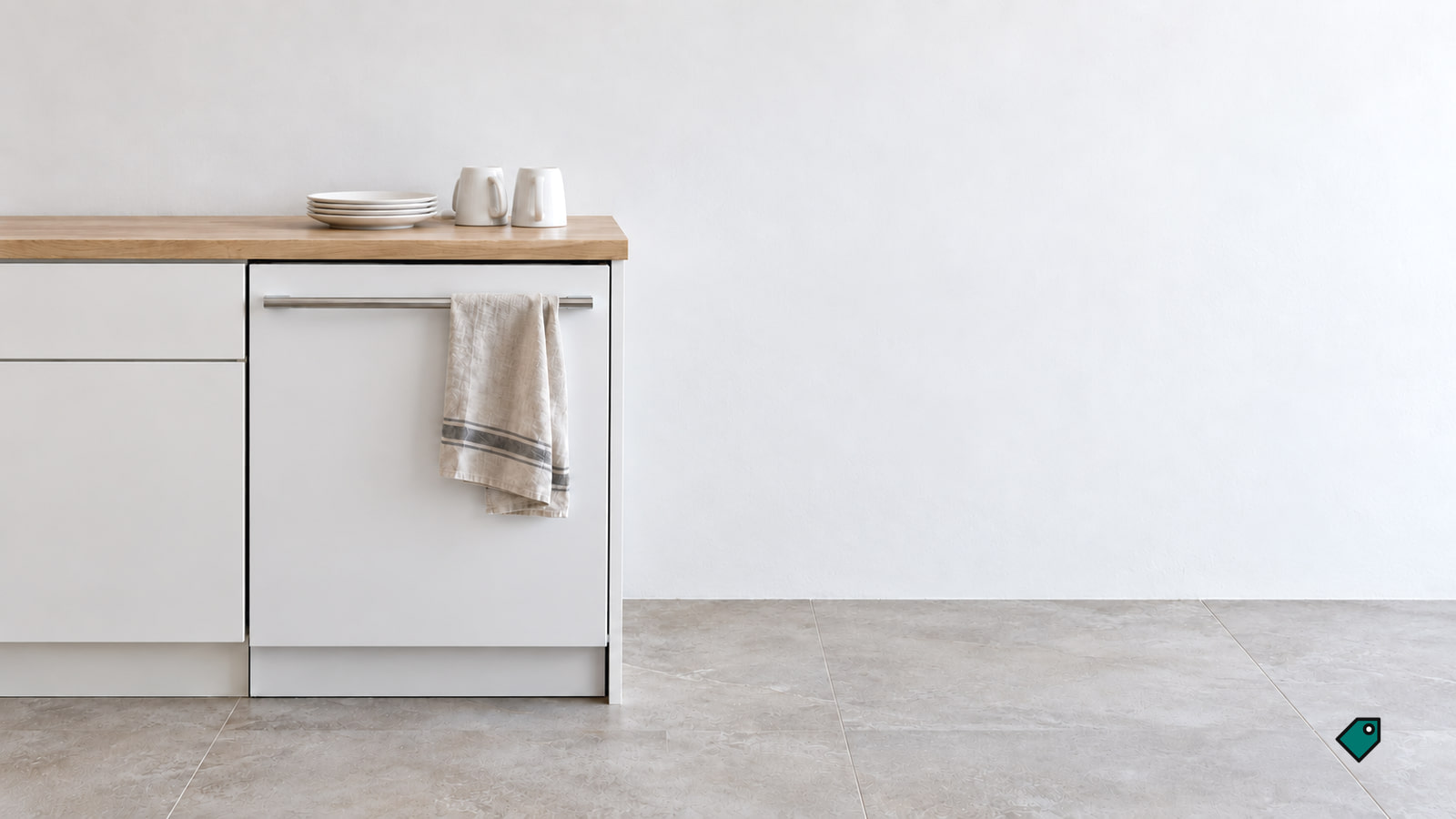 A closed white dishwasher with a towel on its handle sits beneath a wood countertop holding stacked plates and two mugs in a bright kitchen.