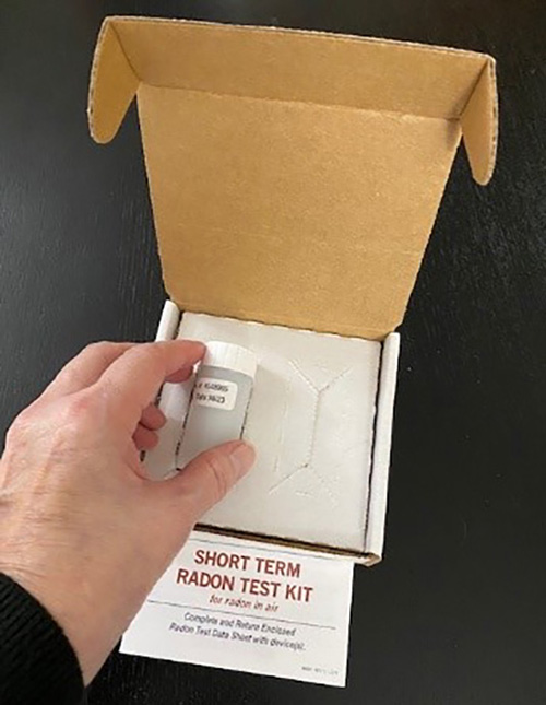 An open short-term radon test kit box with a small sampling device and an instruction sheet labeled “SHORT TERM RADON TEST KIT.”