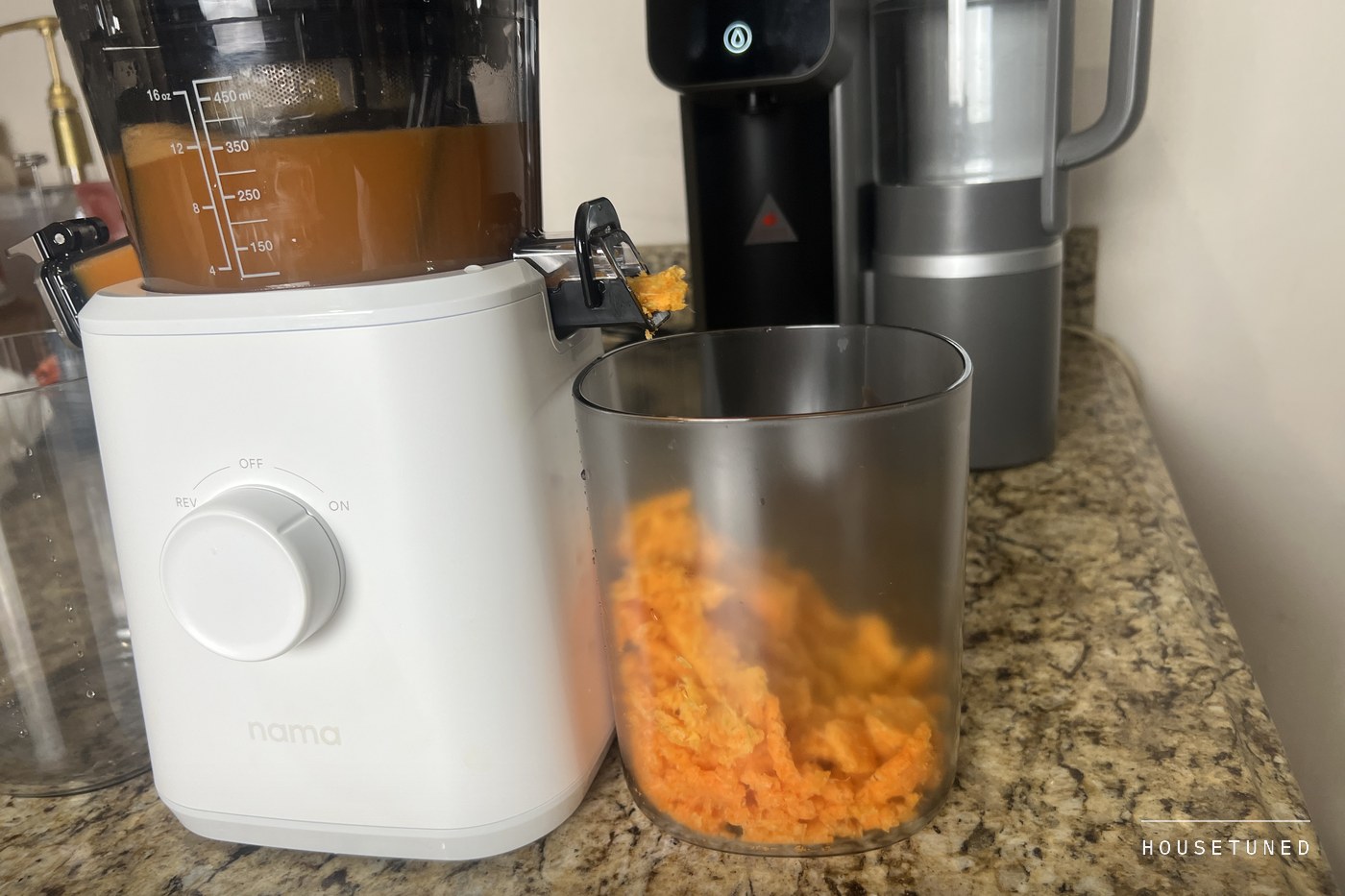 The J2 on a granite counter with orange pulp heaped in the pulp container and juice in the chamber above