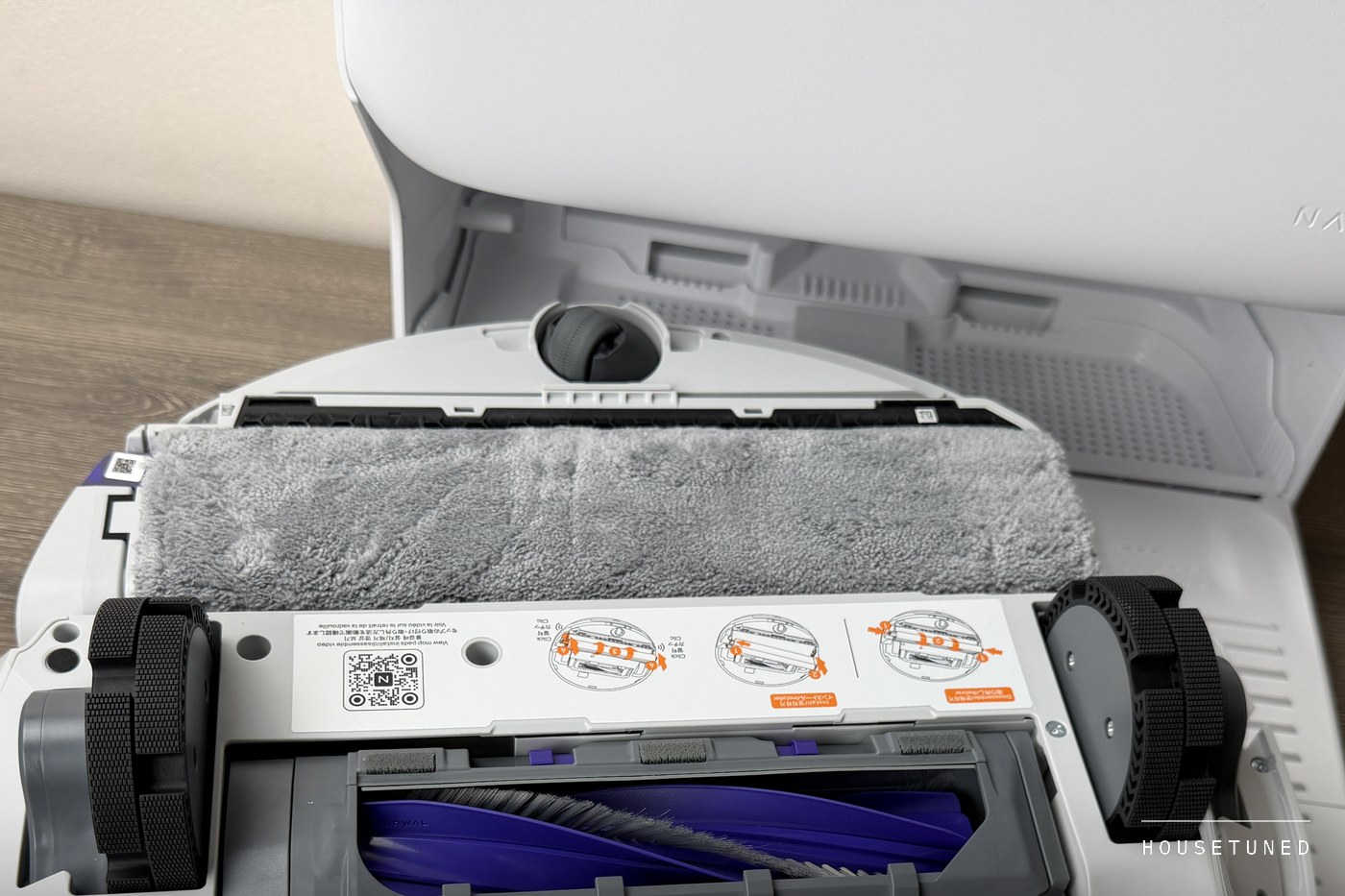 The underside of the Freo 20 Edge: the grey microfibre track mop across the front, the two drive wheels, a mop instruction sticker and the purple roller brush