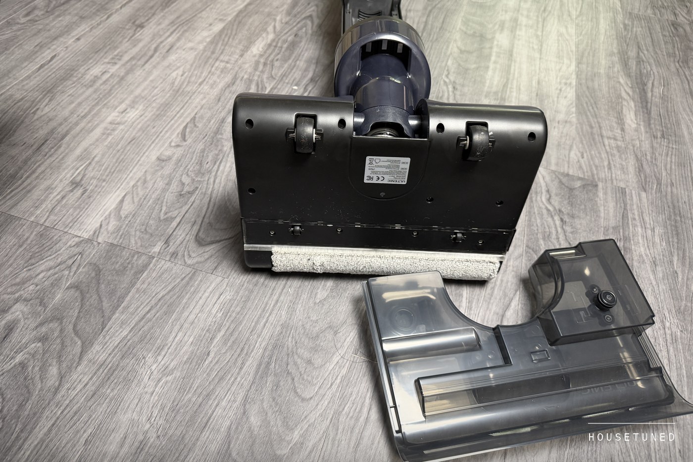 The AC1 TriFlex floor head tipped back on the floor to show its roller, with the head's clear cover lifted off beside it