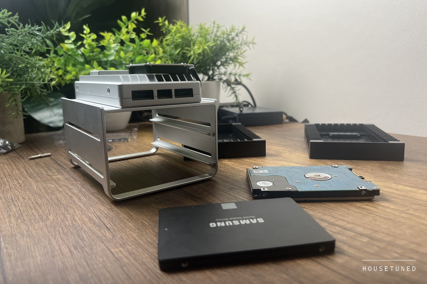 The board in its drive tray on a wooden desk with a Samsung solid state drive and a bare 2.5 inch hard drive laid out in front of it