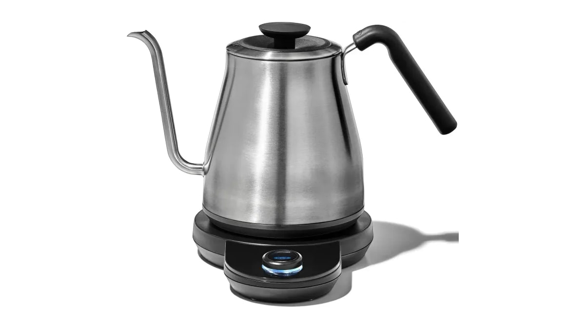 Stainless steel OXO kettle with a curved spout and black handle on its electric base against white.