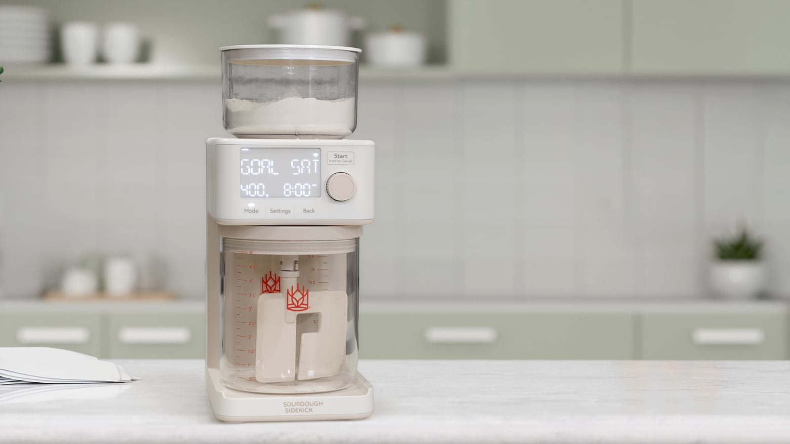 Sourdough Sidekick on a kitchen counter with a flour hopper, digital controls and a clear vessel containing mixing paddles.