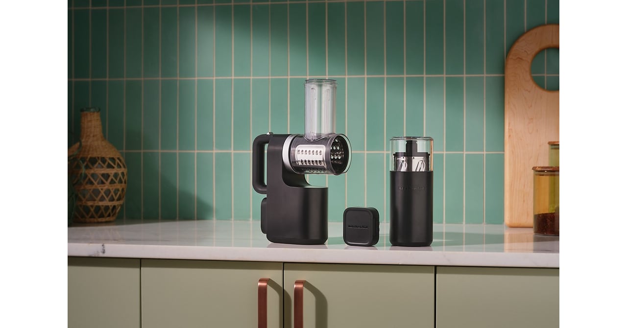 Black KitchenAid cordless grater, battery and accessory storage container on a kitchen counter.