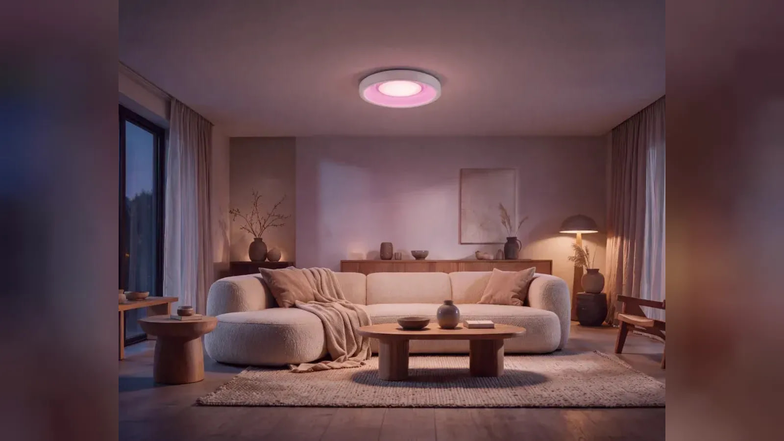 A circular ceiling light glows pink above a sofa, with a lit floor lamp beside it.