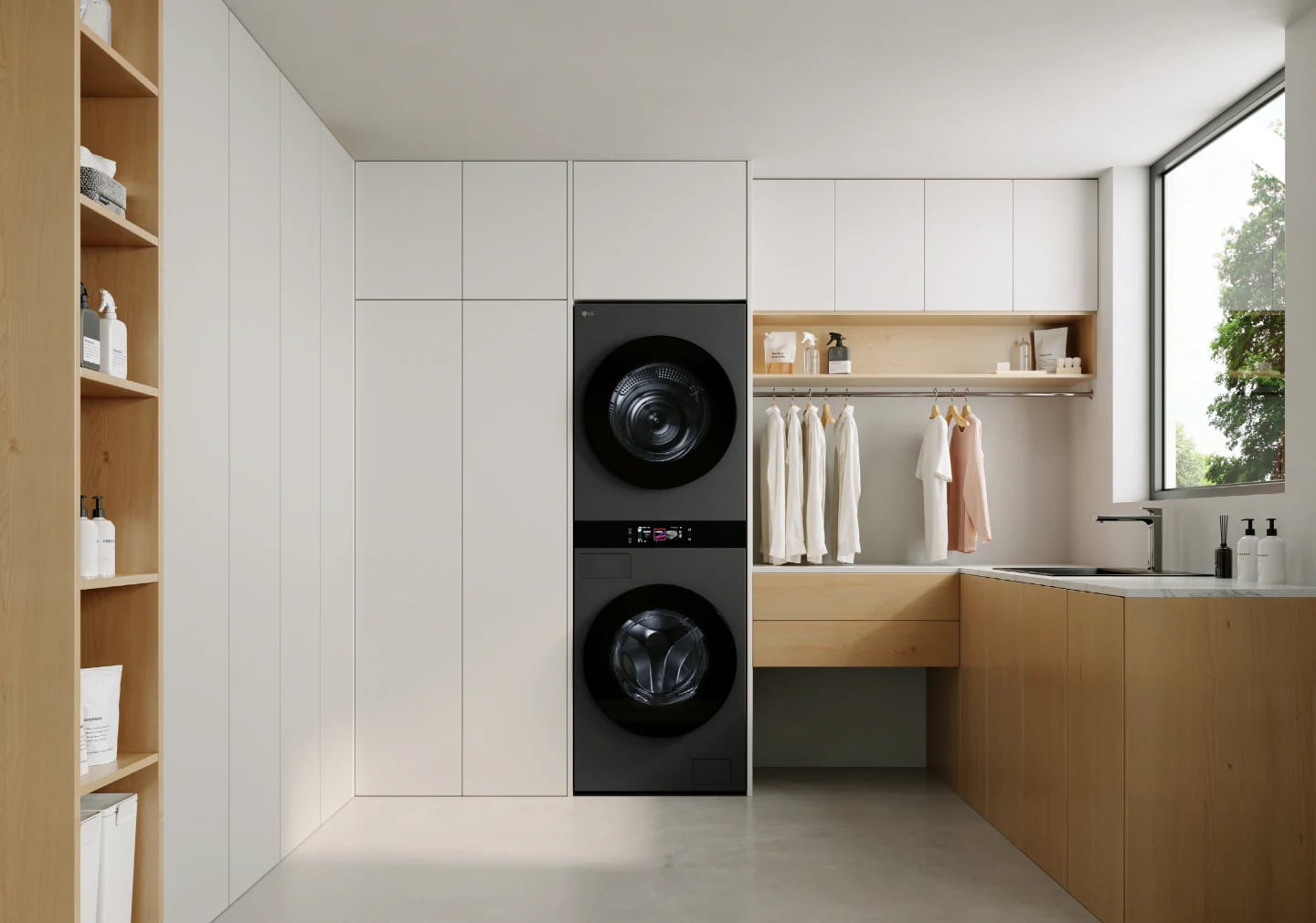 Dark LG WashTower with two stacked drums and central controls beside laundry room cabinets, hanging clothes and a sink.