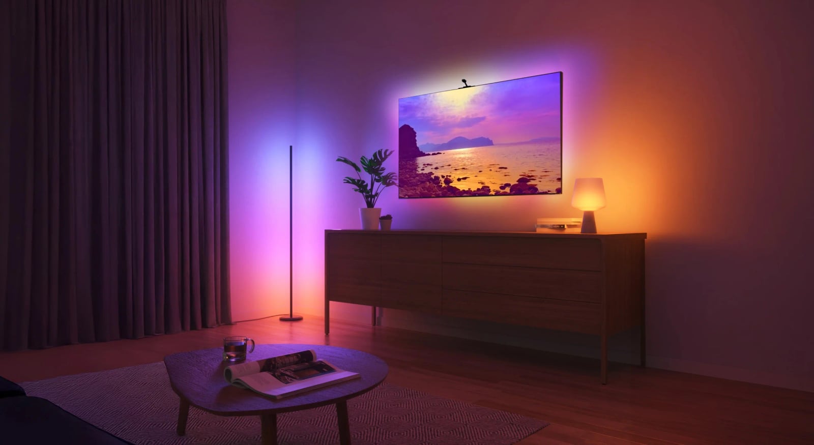 A television displays a sunset above a cabinet, with purple and orange lighting across the surrounding wall.