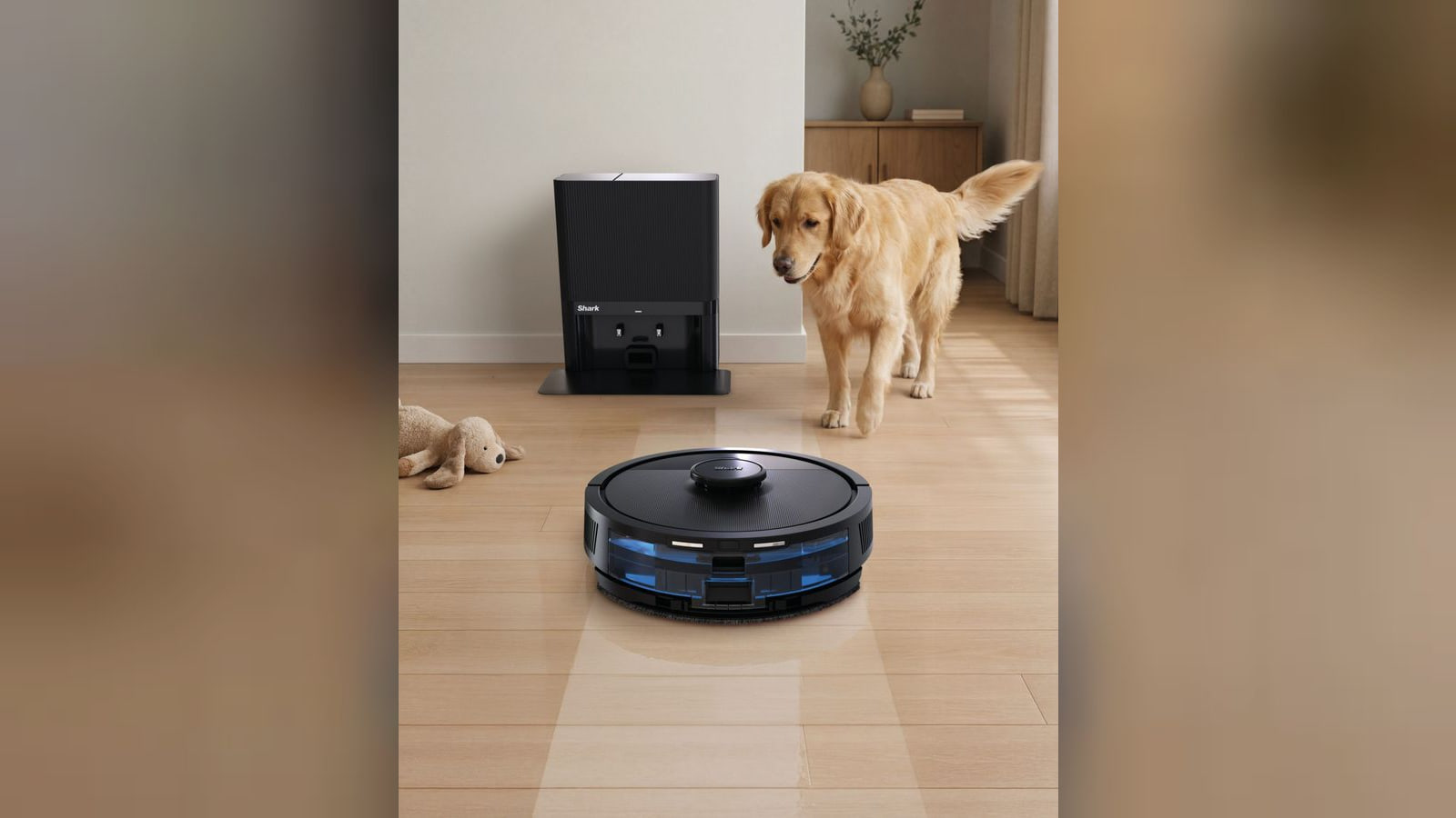 A black Shark robot vacuum and mop on a wood floor with its docking base and a golden retriever behind it.