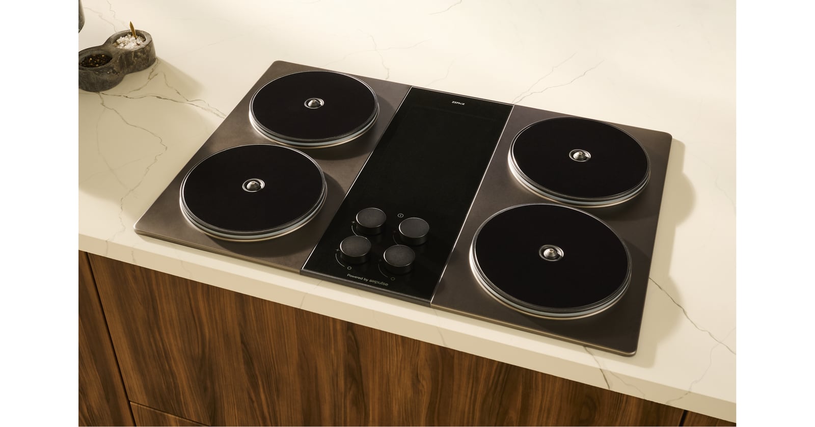 Zephyr cooktop with four circular heating elements and four control knobs set into a light stone countertop.